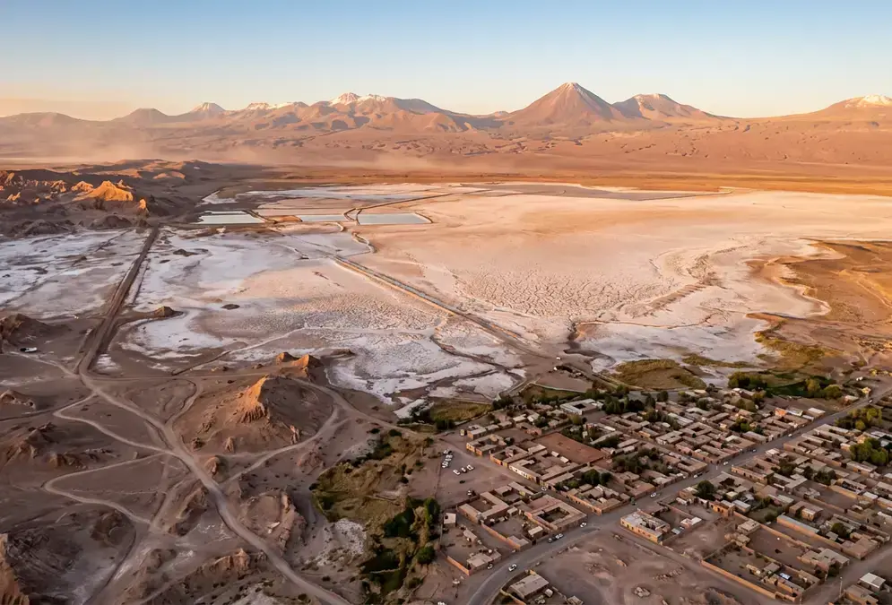 Photorealistic aerial view of San Pedro de Atacama and the Atacama Desert at golden hour, arid salt flat stretching to Andean volcanoes on the horizon, showcasing the 3 to 5 day itinerary landscape