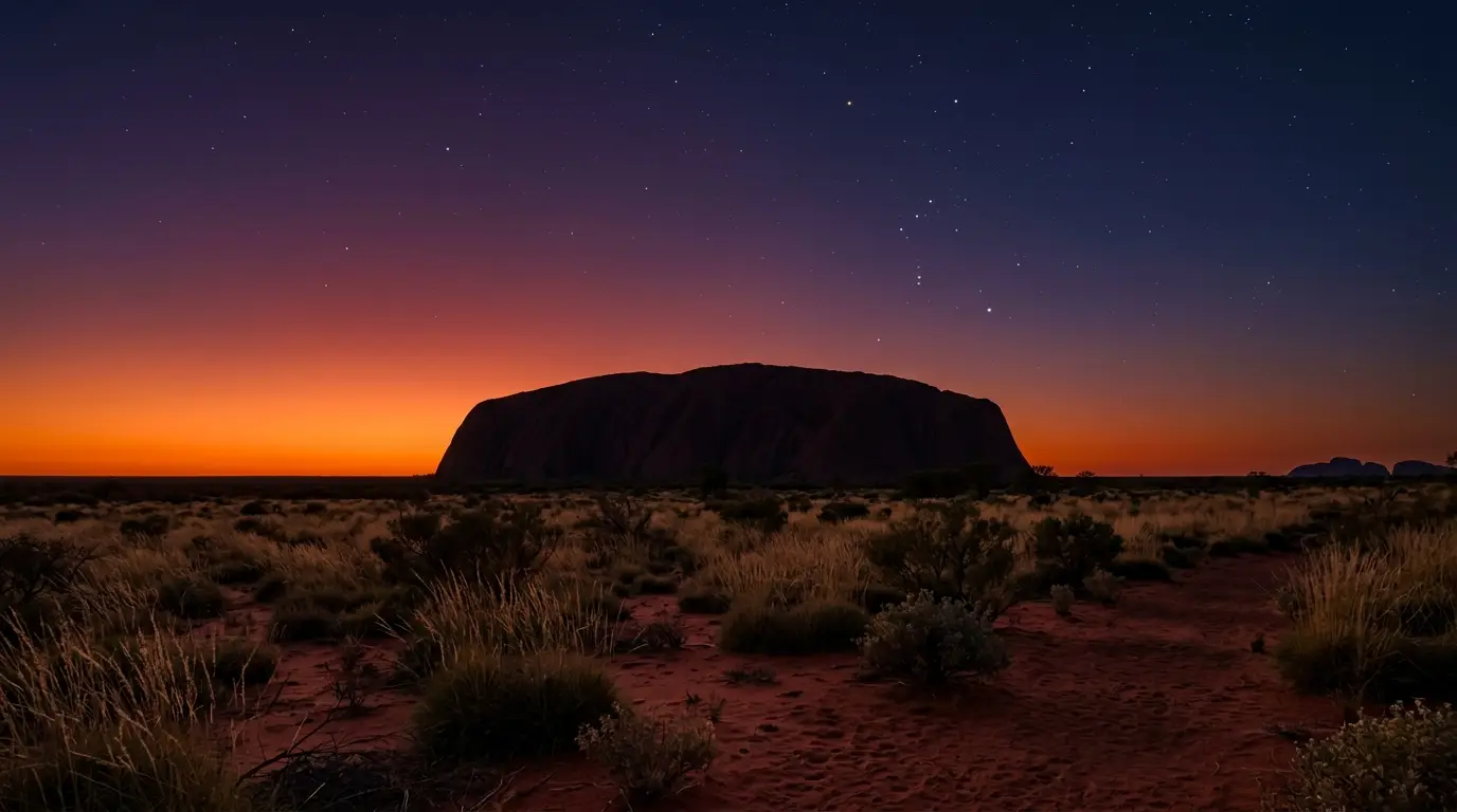 First stars appearing over Uluru's silhouette at dusk, seen from Talinguru Nyakunytjaku, one of the best stargazing spots at Uluru's named viewing areas, red desert sky deepening to violet