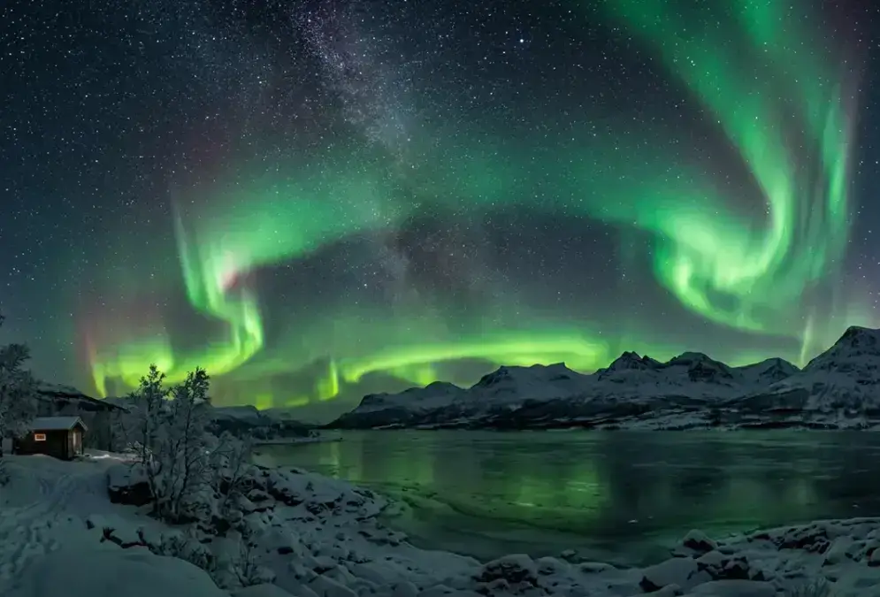Aurora borealis in green ribbons over Lake Torneträsk near Abisko, Swedish Lapland, snow-covered peaks silhouetted against a star-filled sky, illustrating the best time to stargaze in Abisko during deep winter