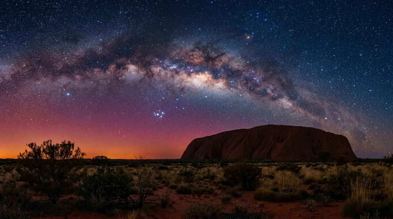 Photorealistic night view of Uluru's silhouette glowing under the Milky Way's galactic core and Southern Cross, red desert sky over Uluru-Kata Tjuta National Park, illustrating how many days a Uluru stargazing trip needs for a clear view like this