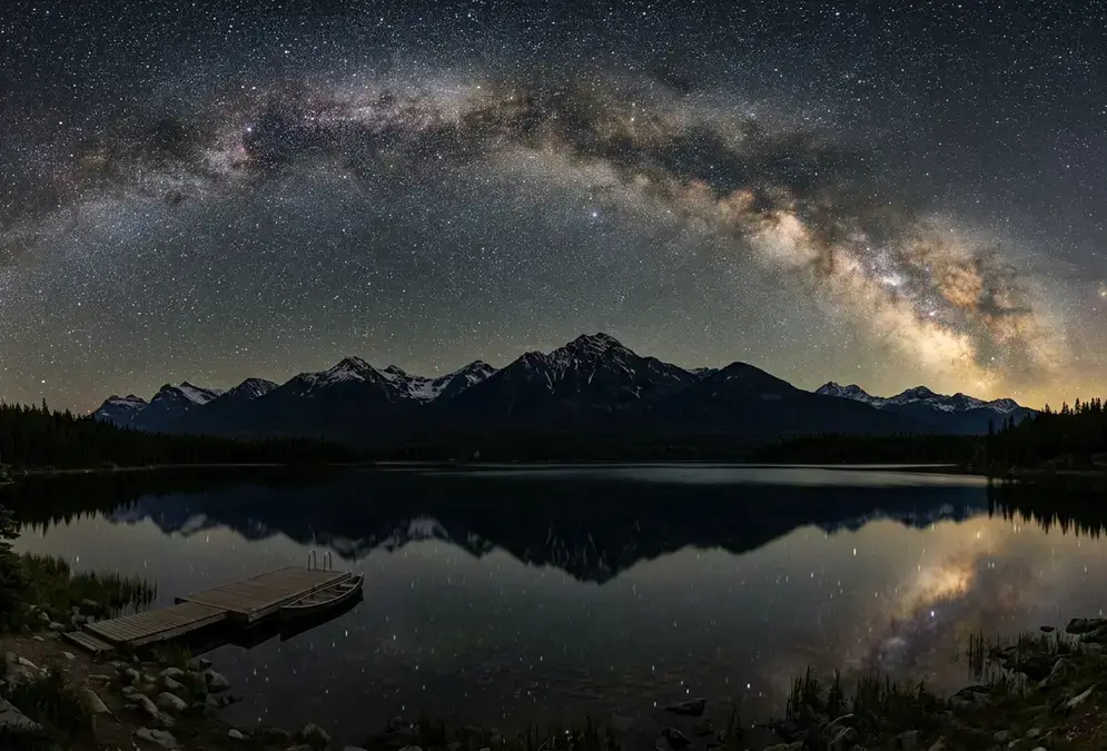 Milky Way arcing over Pyramid Lake in Jasper National Park at night, Rocky Mountain silhouettes reflected in still water under Bortle 1-2 dark sky, the view every Jasper stargazing FAQ points toward
