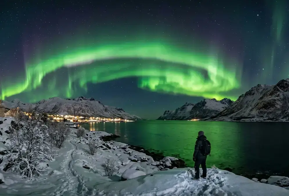 A wide green aurora borealis curtain over a snow-covered Arctic fjord at night in northern Norway, showing the kind of display that happens during a Kp 4 geomagnetic storm, the core concept behind kp index northern lights explained