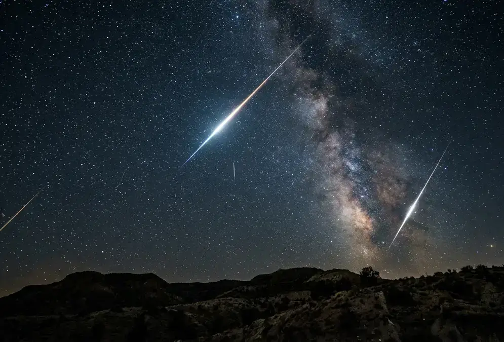 Multiple bright meteor trails streaking across a dark, star-dense night sky above a silhouetted horizon, illustrating a meteor showers guide to the year's best viewing nights