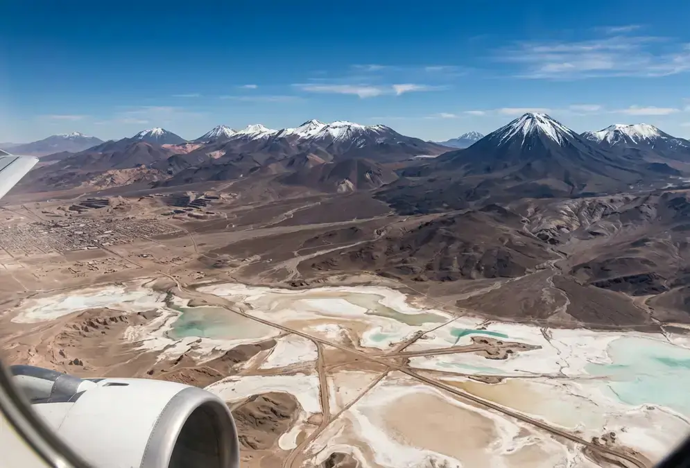 Aerial view of the Atacama Desert from a plane window approaching Calama, Chile, with the Andes volcanoes visible and the salt flats stretching below under clear skies