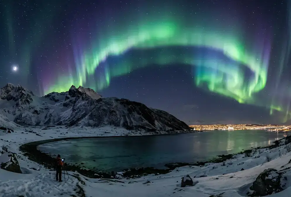 Green aurora borealis curtains arching over a dark Arctic fjord valley at night with Tromsø city lights glowing faintly on the distant horizon, capturing the core contrast in northern lights Tromsø city centre vs outside viewing decisions