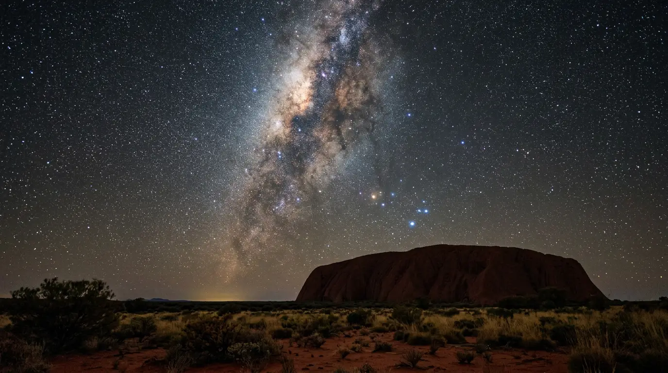 Uluru stargazing: Milky Way galactic core rising over the monolith's silhouette under the Southern Cross, red desert night sky